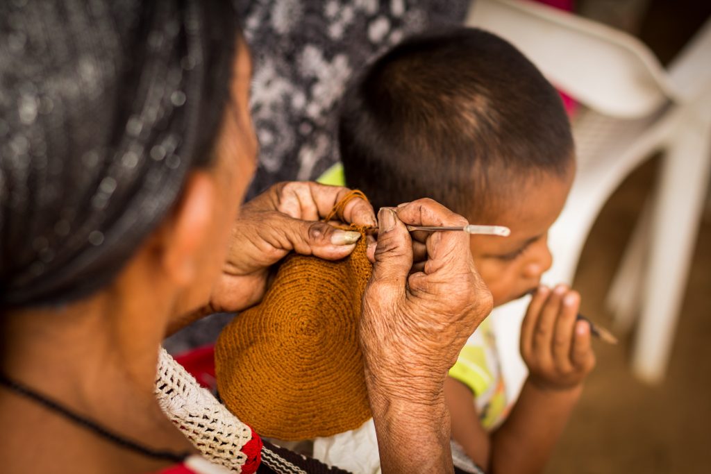 An older Wayuu woman crocheting a brown Wayuu bag with her grandson in a rancheria in La Guajira, Colombia